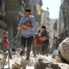 Hombres sirios con bebés en brazos se abren paso entre los edificios destruidos por un ataque aéreo en el barrio de Salihin tomado por los rebeldes en la ciudad de Alepo, el 11 de septiembre.