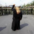 Una mujer de la ciudad de Urumqi, en la región autónoma china de Xinjiang, grita alzando el puño contra la policía paramilitar china mientras se apoya en una muleta.