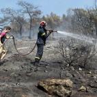 Un bombero y un voluntario tratan de sofocar un incendio en el suburbio de Karea en Atenas (Grecia).