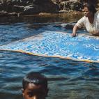 Una mujer nubia lavando su alfombra en el Nilo, mientras su hijo se da un baño. La limpieza es una cualidad famosa de los nubios, probablemente se deba a que viven junto al Nilo, donde pueden limpiar de manera eficaz todas su cosas con agua dulce.