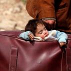 Un hombre traslada toda su vida dentro de una maleta, incluyendo su hijo, que duerme mientras huyen de Ghouta, el principal feudo opositor situado en las afueras de Damasco, Siria.