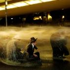 Un grupo de israel&iacute;es ultraortodoxos jud&iacute;os se sientan mientras les echan agua durante una protesta contra la detenci&oacute;n de un miembro de su comunidad que se niega a servir en el ej&eacute;rcito de Israel, en Jerusal&eacute;n.