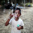Un niño juega con burbujas en un parque de Atenas, donde está su familia, rescatada en las islas griegas