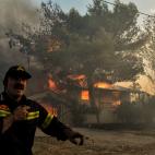 Un bombero busca ayuda mientras una casa se quema a su espalda en Kineta.