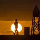 A la par que el sol se pone en el Océano Atlántico, un pescador se prepara para pescar en Bal Harbour, Florida.