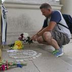 Un hombre deposita un ramo de flores junto a un círculo de velas y otras ofrendas en la entrada de la Embajada de Francia en Londres.