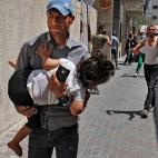 Un hombre palestino huye con su hija en brazos de los edificios bombardeados.