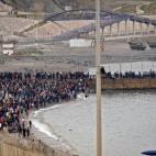 Moroccan migrants rally by a border fence in the northern town of Fnideq in an attempt to cross the border from Morocco to Spain's North African enclave of Ceuta on May 18, 2021, while Spanish troops stand to intercept them on the other side. - ...