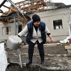 Una mujer trata de recoger lo que queda de una casa pr&aacute;cticamente destruida tras una explosi&oacute;n