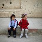Dos niñas se sientan junto a un muro acribillado en el patio de su colegio en la ciudad de Duma, en Damasco.
