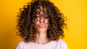 Headshot of girl with curly hairstyle wearing t-shirt send air kiss pouted lips isolated on vivid yellow color background.