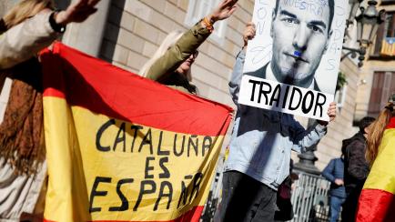 Demonstrators gesture as they hold a Spanish flag reading "Catalonia is Spain" and a defaced image of Spain's Prime Minister Pedro Sanchez reading "Traitor" during a rally in protest against the new coalition government led by Spain's Prime Mini...