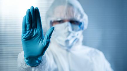 Scientist with hand raised in hazmat protective suit, stop concept.
