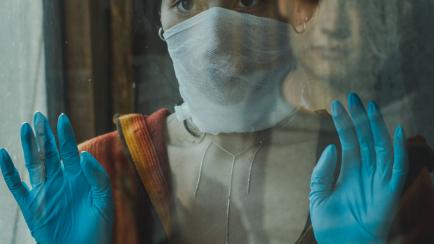 Woman wearing a face mask and protective gloves and looking at the man reflected in the window