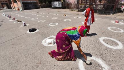 NEW DELHI, INDIA - APRIL 12: A woman placing a container inside circles marked for proper adherence of social distancing at a food distribution by Ramakrishna Mission, on the day nineteen of the 21 day nationwide lockdown to check the spread of ...