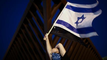 A person with their face covered amid concerns over the country's coronavirus outbreak, waves the national flag during a protest against Prime Minister Benjamin Netanyahu in Tel Aviv, Israel, Sunday, April 19, 2020. More than 2,000 people took t...