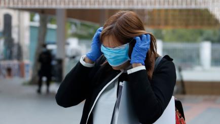 14 April 2020, Spain, Palma: A woman puts on a protection mask outside Palma intermodal trains and bus station during the coronavirus (COVID-19) outbreak in Palma de Mallorca. Factory, construction workers and an increase of transport drivers ar...