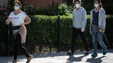 MADRID, SPAIN - MAY 02: A woman running and a couple walk along the city streets wearing face masks on May 02, 2020 in Madrid, Spain.  Spain continues to ease the Covid-19 lockdown measures this weekend, with high temperatures forecast across th...