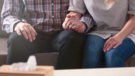 Close-up of a couple holding hands together while sitting on a couch during a therapy