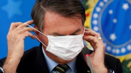 Jair Bolsonaro tratando de ponerse una mascarilla.