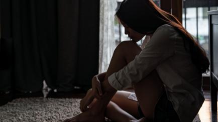 Selective focus loneliness young asian woman sitting on bedroom floor near the balcony. Depression sadness breaking up asian teenage girl sitting alone hugging knees closing eyes and thinking.