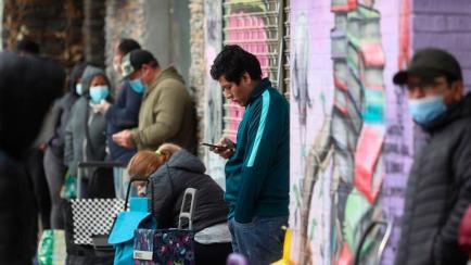 Varias personas esperan en la fila para recoger alimentos proporcionados por la asociación de vecinos de Aluche, en Madrid.
