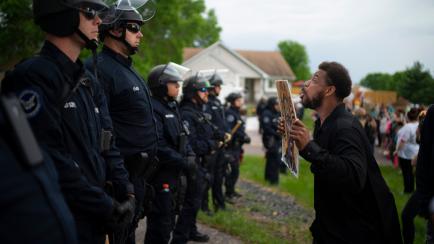 A demonstrator holding a sign jumps up and down so police officers behind the front lines could see it, outside the Oakdale, Minn,, home of fired Minneapolis police Officer Derek Chauvin on Wednesday evening, May 27, 2020. The mayor of Minneapol...