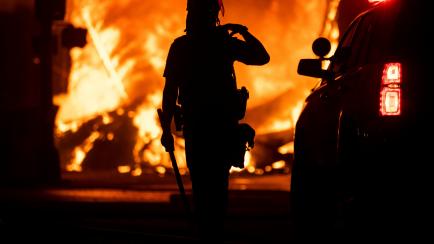 MINNEAPOLIS, MN - MAY 28: A police officer stands watch as a looted pawn shop burns behind them on May 28, 2020 in Minneapolis, Minnesota. As unrest continues after the death of George Floyd fires have been lit in buildings across Minneapolis an...