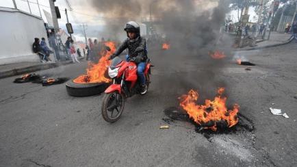 Un motociclista transita por una calle bloqueada con llantas encendidas este jueves durante una jornada de protesta contra las medidas económicas del Gobierno del presidente de Ecuador Lenín Moreno, en Quito (Ecuador). EFE/José Jácome