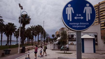 Una familia en el paseo marítimo de la Malagueta (Málaga) ante un disco que recuerda mantener la distancia de 2 metros entre personas, este domingo.