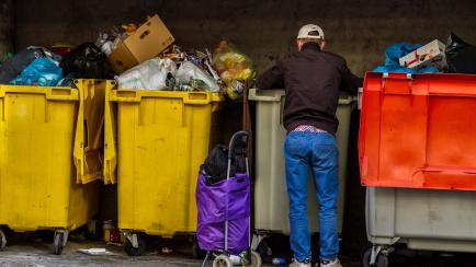 Madrid, Spain - May 02, 2020: Adult man searches for food in the garbage with a mask for the coronavirus COVID-19 in the Vicálvaro neighborhood in Madrid