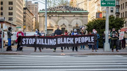 Un grupo de personas sostiene una pancarta que dice "dejar de matar en las personas negras" en una vigilia en Manhattan en honor a George Floyd.