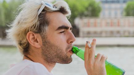 Imagen de archivo de un joven bebiendo cerveza mientras que fuma un cigarrillo.