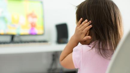 A child watching tv holding her ears because she is afraid of the sound; Child behavior theme