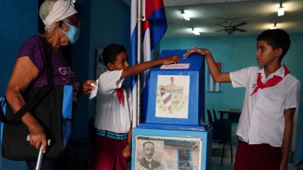 Unos niños ayudan a una mujer a depositar su voto en la urna. 
