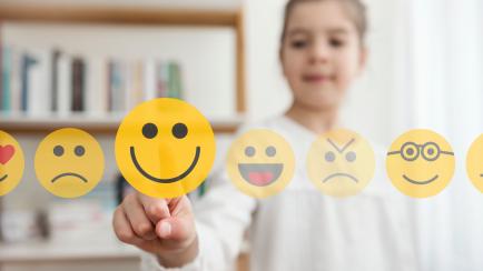 Una niña, señalando emociones representadas como 'emojis'.