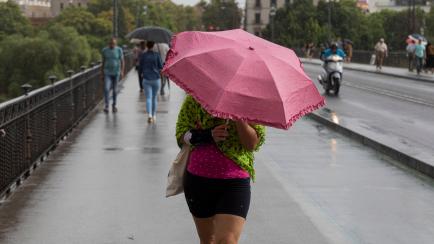 Una viandante se cubre con el paraguas en Sevilla.