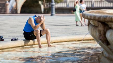 Un hombre se refugia del calor en una fuente de Sevilla.