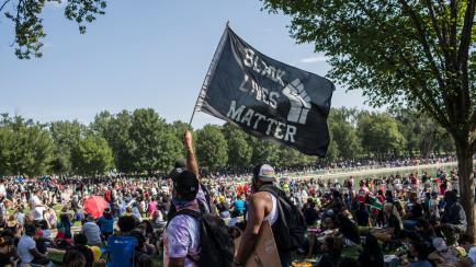 WASHINGTON, DISTRICT OF COLUMBIA, UNITED STATES - 2020/08/28: A demonstrator holding a flag with Black Lives Matter written on it while attending  the "Commitment March: Get Your Knee Off Our Necks" protest against racism and police brutality at...