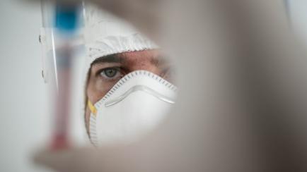 in a chemistry lab, a male researcher holds a tube with the coronavirus virus