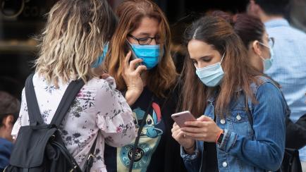 Three young women wearing masks to help prevent the spread of coronavirus stand together using their phones in Madrid, Spain, Thursday, Oct. 8, 2020. A court in Madrid has struck down a national government order that imposed a partial lockdown d...