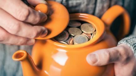 Close up of mans hands holding teapot full of coins