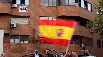 Acto de Vox en Vallecas. De fondo, una vecina se asoma junto a un cartel contra el partido de ultraderecha.