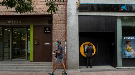 MADRID, SPAIN - SEPTEMBER 17: A man walks past branches of Bankia (L) and CaixaBank (R) on September 17, 2020 in Madrid, Spain. The Caixabank and Bankia merger will create Spain's biggest lender, with a market value of about 16bn euros and hold ...
