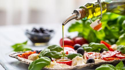 Pouring olive oil on caprese salad. Healthy italian or mediterranean meal.
