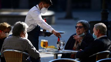 A waiter serves customers at a restaurant in Barcelona on November 23, 2020 as bars, restaurants and movie theatres were allowed to reopen in Spain's northeastern region of Catalonia after being closed for over a month as part of measures to slo...