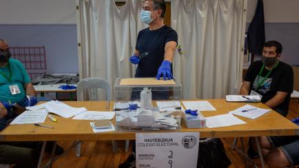 SAN SEBASTIAN, SPAIN - JULY 12: Polling clerks, wearing medical masks and gloves, wait for a person to put their vote in the ballot box to elect representatives to the Basque regional parliament during elections for the autonomous parliaments of...