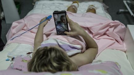 Una niña mira un móvil en una cama de hospital