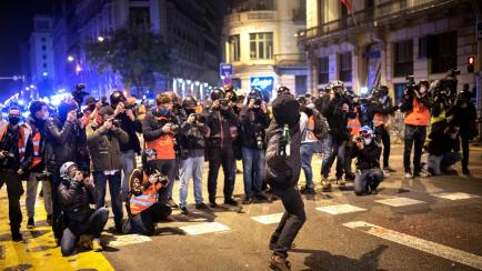 Un grupo de fotógrafos toma imágenes de un hombre que arroja una botella contra una comisaría de policía durante las protestas contra la detención del cantante Pablo Hasél en Barcelona.