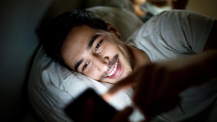 Un joven mira el móvil en la cama.